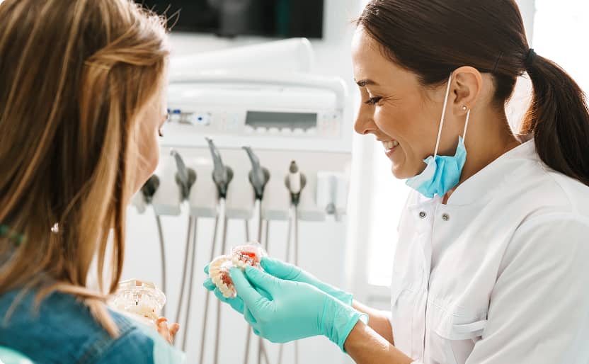Clayton Smiles | Dentist smiling while showing a young patient a dental model during a consultation
